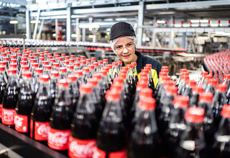 Coca-Cola Mitarbeiterin wirft prüfenden Blick auf Flaschen in der Produktion