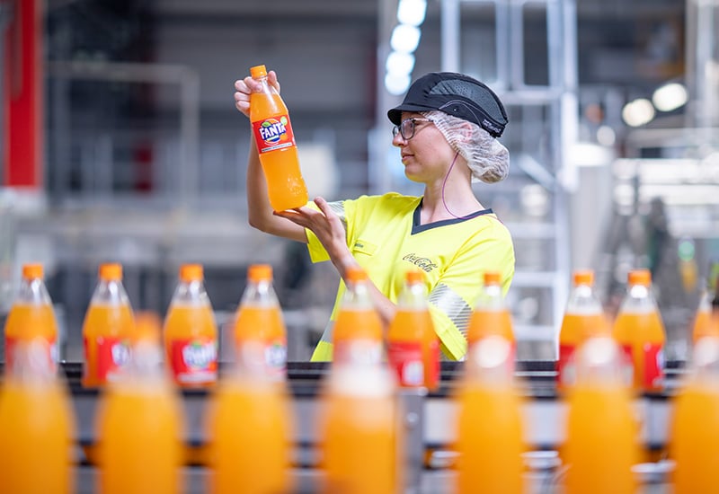 Coca-Cola Mitarbeitende bei der Überprüfung einer Fanta Flasche