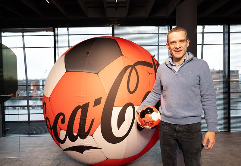 John Galvin im Headquarter von Coca-Cola Europacific Partners Deutschland in Berlin - mit einem Fußball zur EM in der Hand
